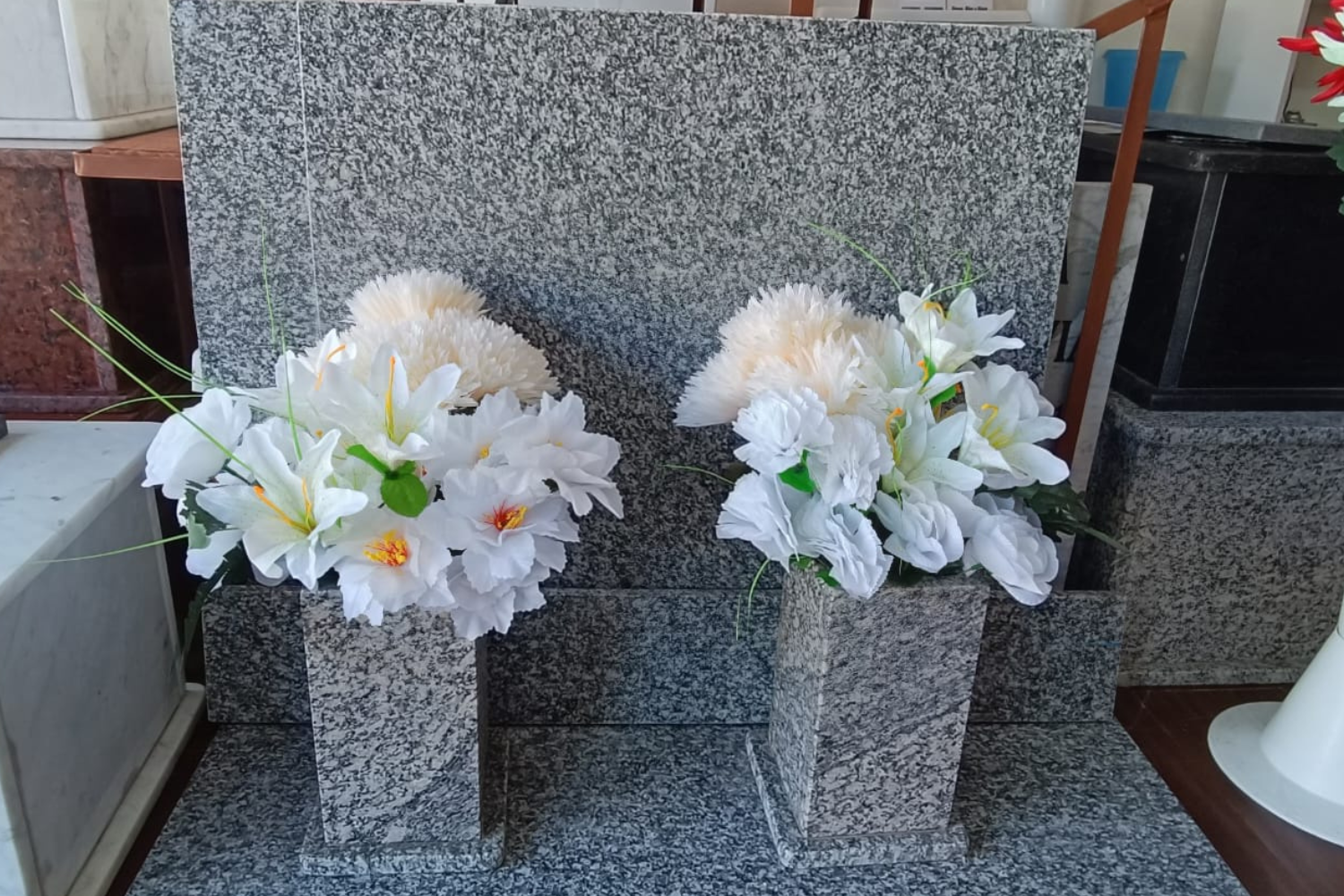 Lápida de granito gris con floreros y arreglos florales blancos